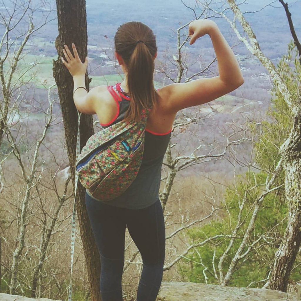 girl posing with arm flexed on mountaintop where they went walking