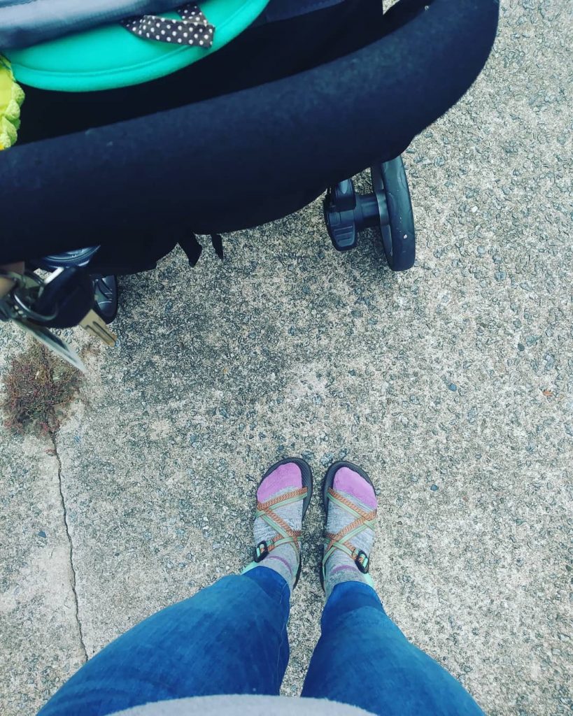 girl wearing socks and chacos while pushing stroller while walking