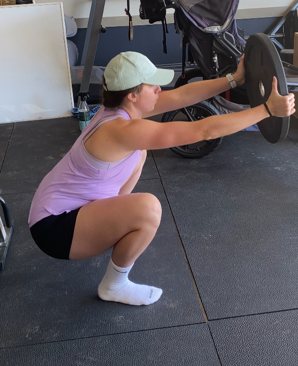 personal trainer demonstrating postpartum safe exercise with barbell plate wearing purple workout tank and mint hat. Women with muscles.